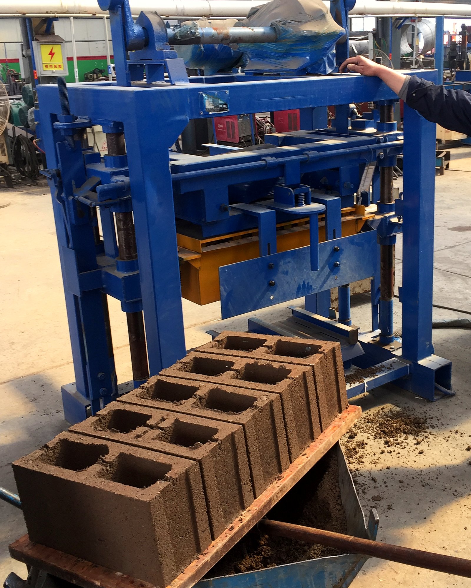 Blue manual concrete block machine with freshly pressed hollow blocks on a pallet