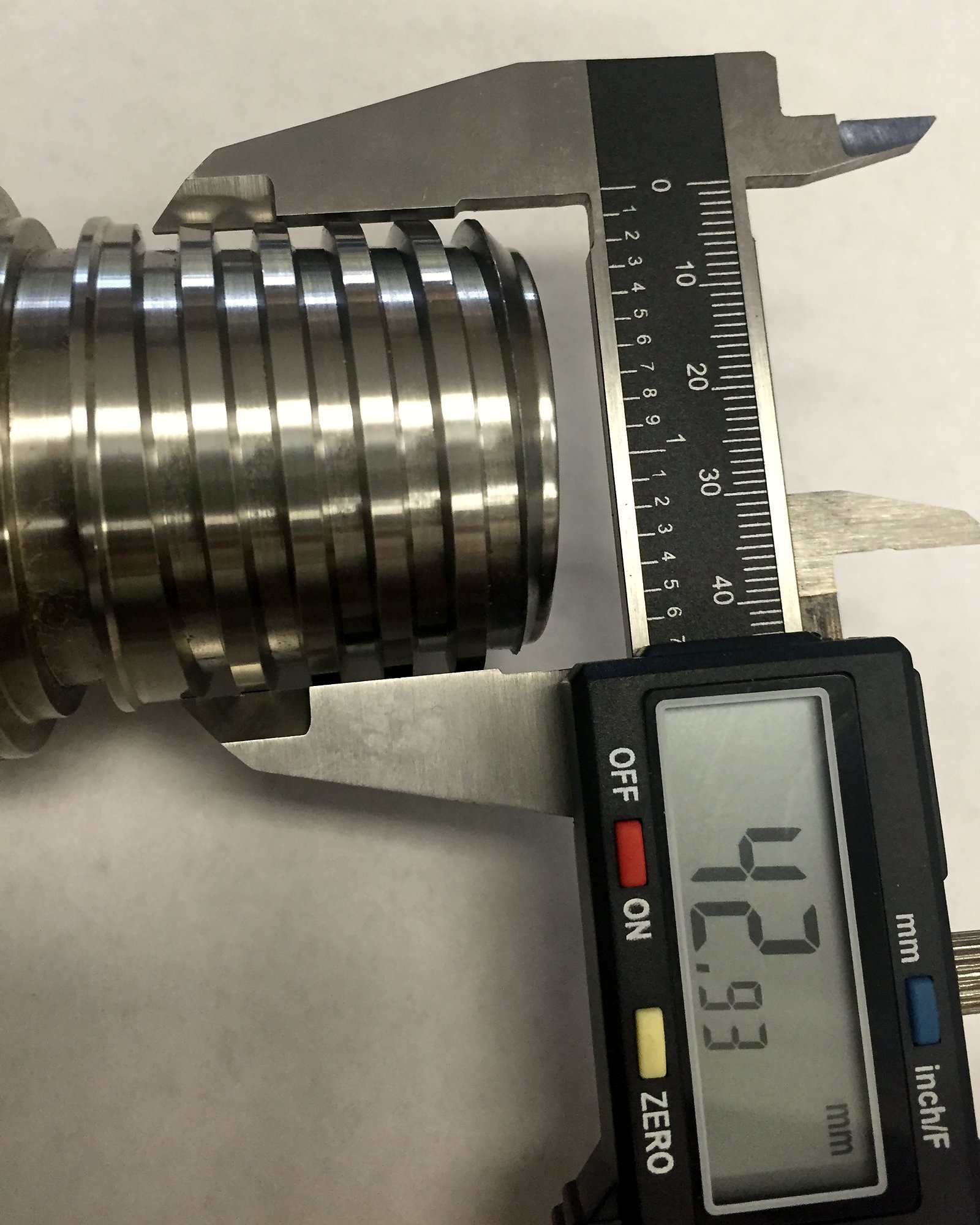 Digital caliper reading 42.93 mm across a machined steel part