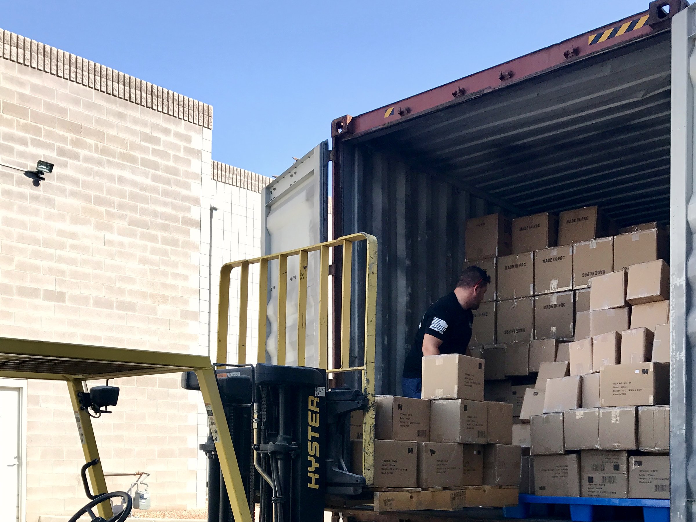 Forklift beside an open shipping container stacked with cartons marked Made in PRC
