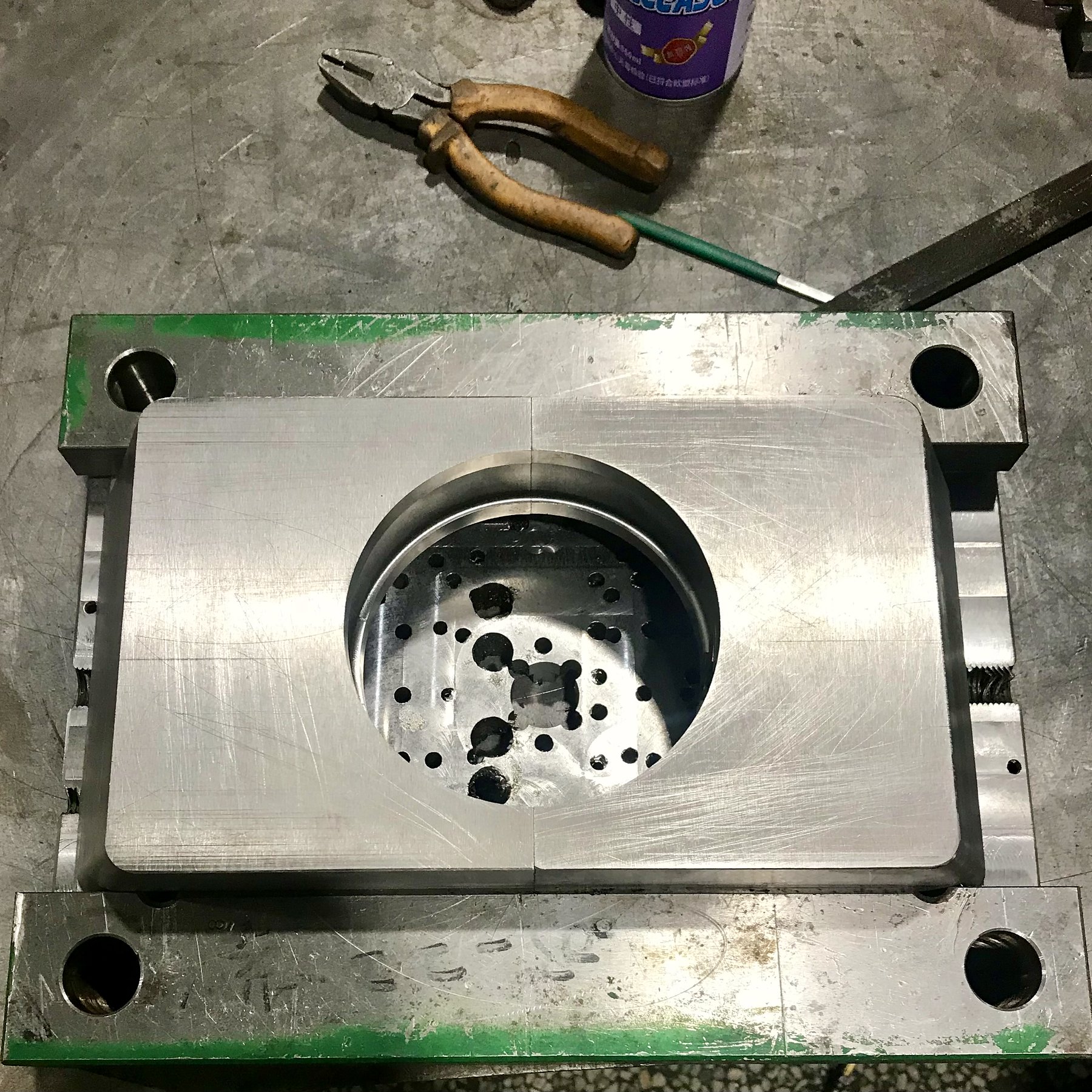 Open steel injection mold base on a workbench with pliers and a file